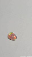 Photo showing pear-shaped cabochon Ethiopian opal with visible green and orange spectral flashes on a white background.