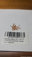 Photo of 56 calibrated round brilliant orange yellow sapphires, labeled with total carat weight 1.73ct and size 1.7mm each.