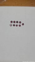 Top view of 10 round cut blood red rubies arranged in two rows on a white background showing their deep color and size.