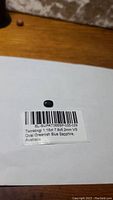 Oval greenish-blue sapphire gemstone placed on a white label showing barcode and description, measuring 7.6x5.2mm with VS clarity and 1.18ct weight from Australia.