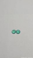 Two round green cabochon emeralds side by side on white background