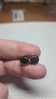 Front view of both earrings held between fingers showing round faceted black stones