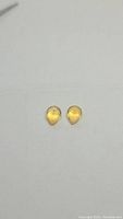 Pair of pear-shaped golden citrine gemstones lying flat on a plain surface, showing size and shape.