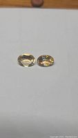 Pair of oval-cut golden citrine gemstones placed side by side on white background, showing size, shape, and color.
