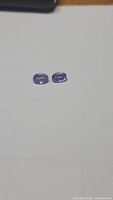 Two small oval faceted tanzanite stones placed on a plain surface, showing their purple color and oval shape