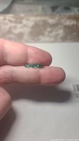 Three oval cut Zambian emeralds of bright green color and high luster shown on fingers for scale