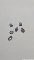 Photo showing seven oval cut untreated fancy exotic sapphires with various purple and blue color tones. Stones are arranged loosely on a white background to display clarity and color.
