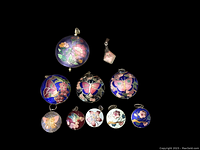 Top-down photo of 10 vintage painted enamel cloisonné pendants arranged flat on black background with floral and butterfly designs in various colors