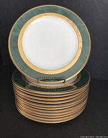 Photo showing the stack of 12 Noritake Fitzgerald salad plates with green and gold ornate borders and a stand holding one plate upright.