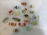 Top-down view of 17 colorful art glass candy figurines arranged on white surface.