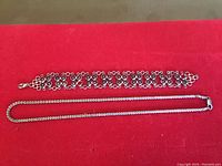 Top view of the silver bracelet and silver necklace laid flat on a red surface.