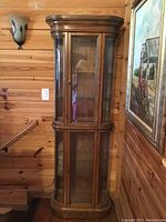 Full view of the oak curio cabinet showing curved glass sides and wooden frame. The cabinet is against a wooden paneled wall near a painting.