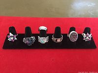 Full view of seven sterling silver rings on display with various designs including floral and butterfly motifs, embellished with faux stones and enamel