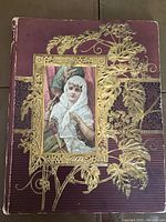 Image of the scrapbook's front cover showing a purple background with elaborate gold embossed floral designs and a central portrait of a Victorian woman in lace.