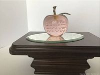 Clear pink glass apple paperweight with brass stem and leaf on a mirrored surface.