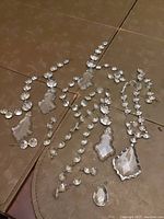 Overall layout of assorted vintage chandelier crystals arranged on floor, showing various crystal shapes and sizes