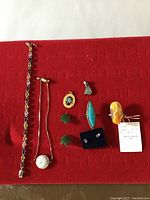 Full view of assorted jewelry laid on red fabric showing bracelet, pendants, rings, earrings, and chain.