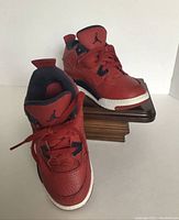 Single pair of red and black Nike Air Jordan Retro 4 SE FIBA kids shoes on a wooden stand, front angled view