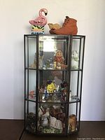 Overall view of glass curio shelf filled with multiple small vintage miniature figures showing various sides