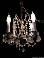 Frontal close-up showing gold-tone metal frame, crystal drops, and lit candle-shaped bulbs.