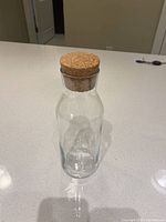 Clear glass juice container with natural cork stopper placed on a white countertop.