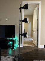 Full view of floor lamp with three black adjustable lampshades on a black metal pole in a living room setting.