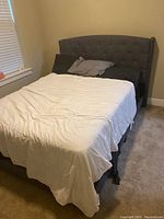 Full view of the queen sized bed with grey upholstered tufted headboard, white bedding and pillows, showing its condition and setup.