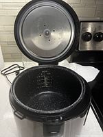 Open rice cooker showing non-stick inner pot with water level markings inside and open lid with heating element visible.