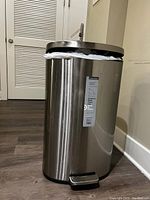 Steel trash can with a pedal at the base, stainless steel body with a black lid and base. The bag liner is visible and the pedal mechanism appears intact.