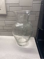 Clear glass vase positioned on a white countertop against a tiled backsplash with minor reflections visible on the glass surface.