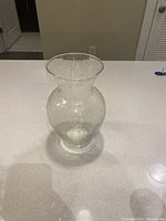 Clear glass flower vase with bubble texture and flared opening on a white countertop.