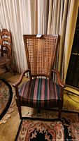 Front view of tall cane back armchair with woven cane back and colorful striped padded seat