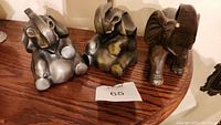 Three elephant figurines on wood surface; two pewter bookends and one brown ceramic elephant