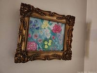 Photo showing the framed floral painting on canvas hung on a wall, highlighting detailed carved gold-tone frame and the colorful floral artwork.