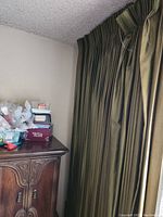 Photo showing the golden metallic green drapes fully hung from ceiling to floor in a room with a textured ceiling and furniture beneath the window.