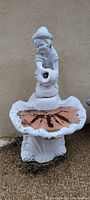 Cement garden fountain approximately 5 feet tall featuring a child figure pouring water from jug into clamshell basin.