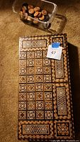 Top view of closed inlaid wooden game box with geometric patterns and sets of playing pieces in container.