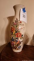 Front angled view of the tall cream vase showing colorful hand painted flowers and birds.