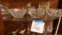 Photo showing six heavy leaded crystal bowls of various sizes and cut patterns, including a covered candy dish with a lid and knob, arranged on a glass shelf.