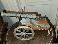 Side view of metal replica cannon matchbox showing detailed rivets, wheels and leather-like patches on carriage.