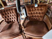 Two mid century carved wood armchairs with tufted brown velvet cushions and cane sides, showing cushion and backrest details.