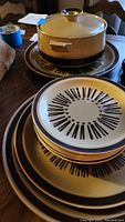 Set of brown stoneware with starburst pattern plates stacked around a stoneware covered casserole dish