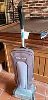 Photo of one Oreck upright vacuum cleaner, showing its upright position, fabric dust bag with logo, and metal handle with black grip