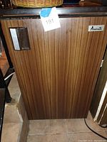 Photo of the full front door of the small brown Avanti mini fridge with wood-grain finish and handle.