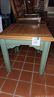 Small farmhouse side table with natural wood plank top and green painted legs on tile floor. Shows front and side detail.