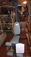 Front view of weight bench showing padded seat, backrest, handles, leg supports, and attached exercise chart note.