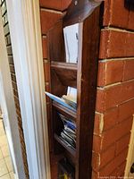 Side angle photo showing the three vertical compartments of the wooden mail sorter filled with papers and mail, mounted on a wall next to a doorway with a brick wall in the background.