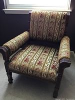 Front view of antique wood frame armchair with patterned jacquard upholstery showing carved wood arms and legs.