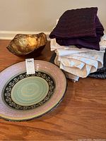 Photo showing two decorative bowls and a stack of folded table linens on a wood floor.