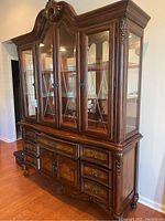 Front angle view of the china cabinet showing ornate carved wooden frame, glass doors with muntins, shelves inside, bottom drawers and doors.